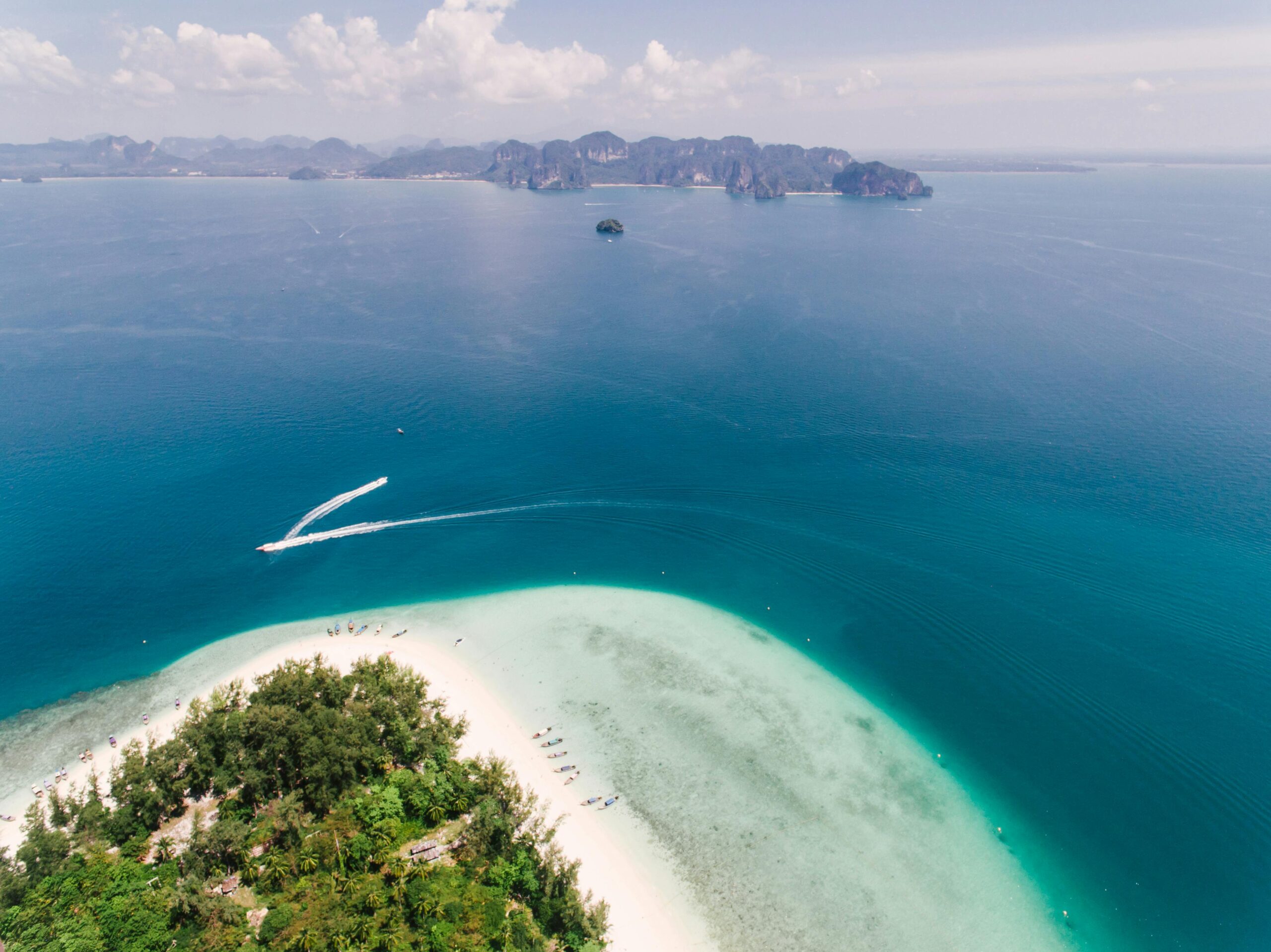 Stunning aerial view of a tropical beach with a speedboat on clear blue ocean waters.